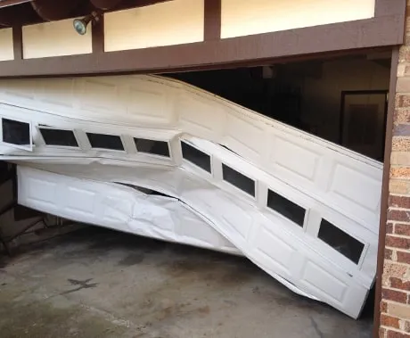 Damaged white sectional garage door before the work