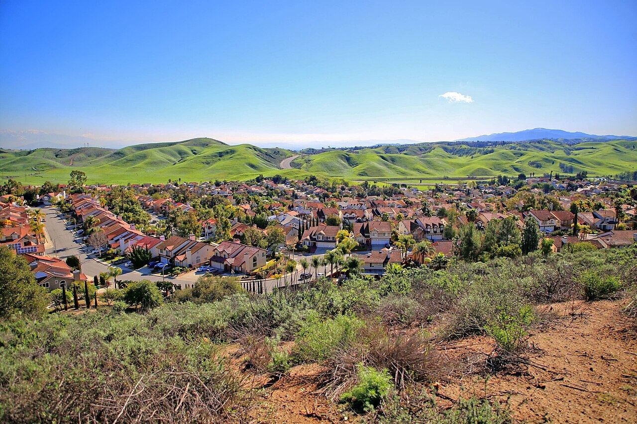 Rows of homes and garages below green rolling hills.